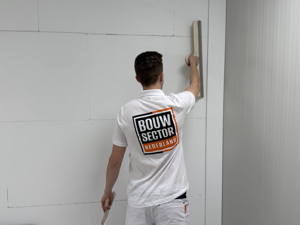 Vakman van Bouwsector Nederland strijkt een wand vlak met een lange spaan